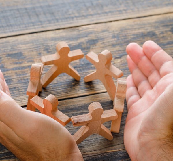 Business success concept on wooden background high angle view. hands protecting wooden figures of people.